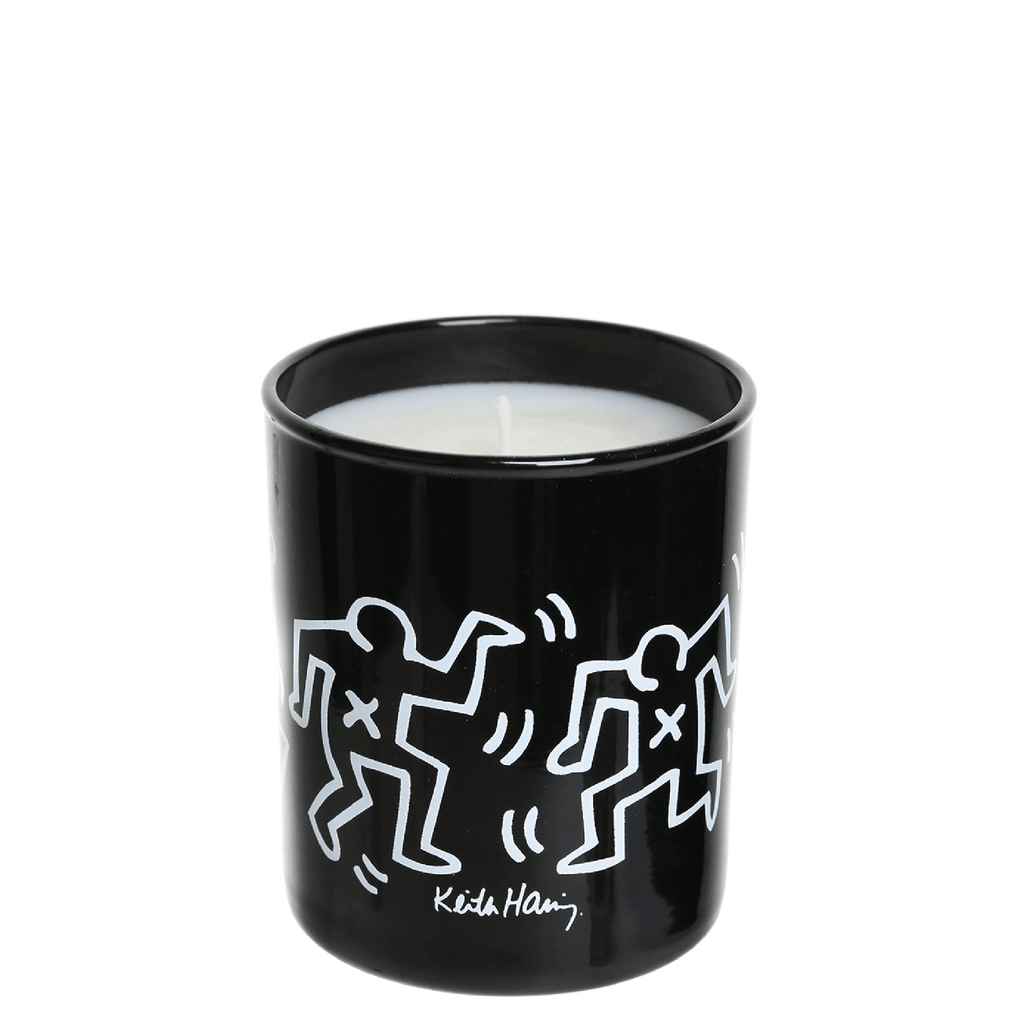 White background with a black container. The container has white markings with dancing characters and an inscription of Keith Haring. The container holds a scented candle made by Ligne Blanche Paris.